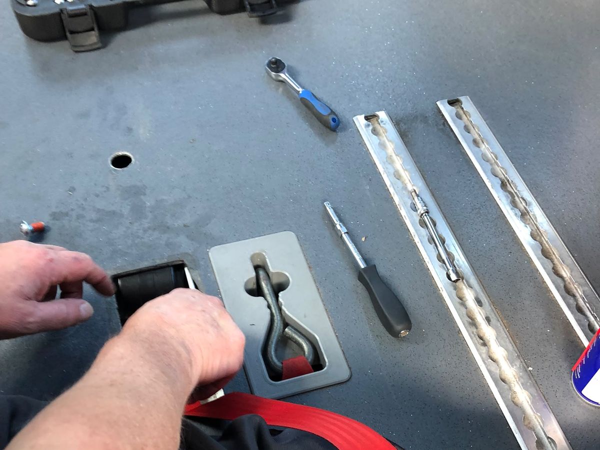 Gerard werkt aan een vergrendeling in de vloer van een rolstoelbus, met de spanband waarmee de rolstoel vastzit